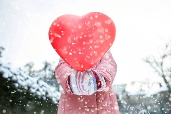 image of a happy joyful smiling woman happily walking outdoors at frosty snowy winter day with a heart shaped red balloon