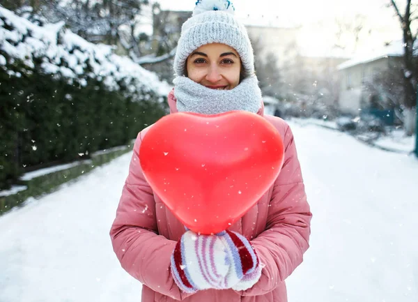 Immagine di una felice donna gioiosa sorridente che cammina felicemente all'aperto in una gelida giornata invernale innevata con un palloncino rosso a forma di cuore — Foto Stock