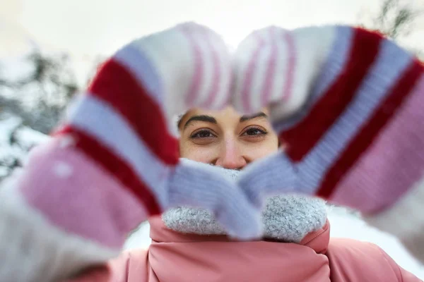 在严寒的冬日 穿着粉红色冬季帕卡 针织帽和围巾在户外散步的快乐快乐微笑的女人 女人用双手示意心脏 — 图库照片