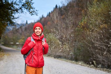 kırmızı ceket ve dağlar arka plan üzerinde duran turuncu pantolon giyen kadın uzun yürüyüşe çıkan kimse ile sırt çantası,