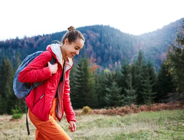 Nainen retkeilijä reppu, yllään punainen takki ja oranssi housut, kävely vuorilla — kuvapankkivalokuva