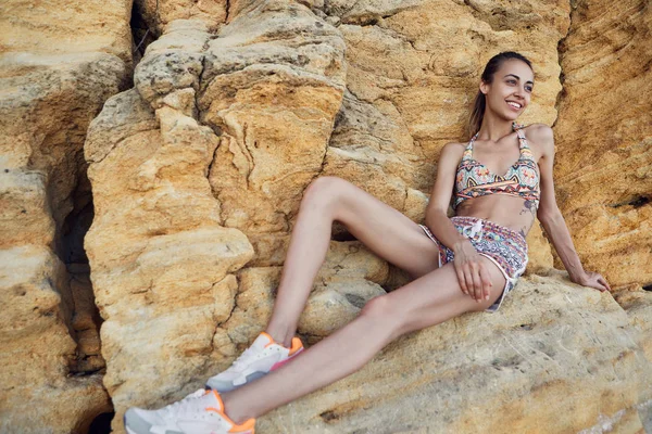 Atleet jonge vrouw die zich voordeed op de rotsen bij het strand. Gelukkig brunette vrouw met fit lichaam in sportkleding — Stockfoto