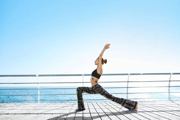 Foto de una joven deportista haciendo ejercicios de yoga en la playa . — Foto de Stock