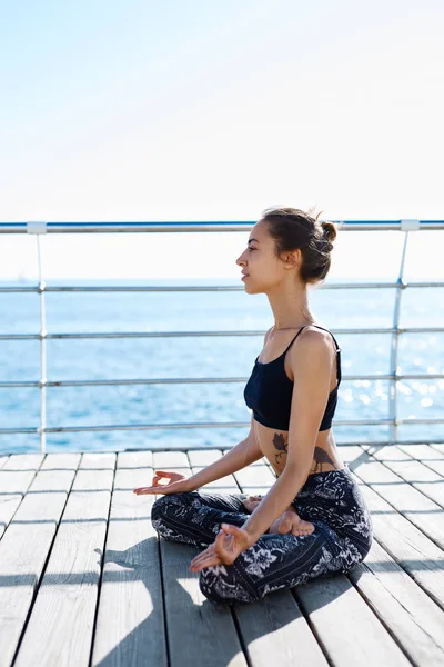 Porträtt av en vacker ung kvinna som sitter i lotus pose vid stranden med havet bakgrund. Känna sig så bekväm och koppla av. — Stockfoto