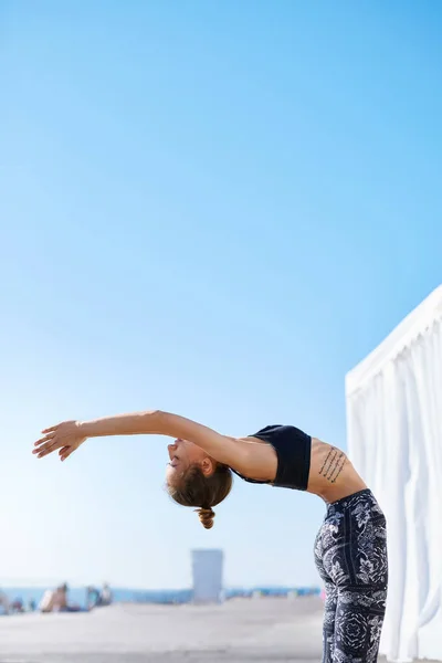 Foto de una joven deportista haciendo ejercicios de yoga en la playa . — Foto de Stock