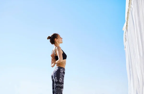 Photo of young sports woman make yoga exercises and stretching on seaside against blue sky. Feeling so comfortable and relax.