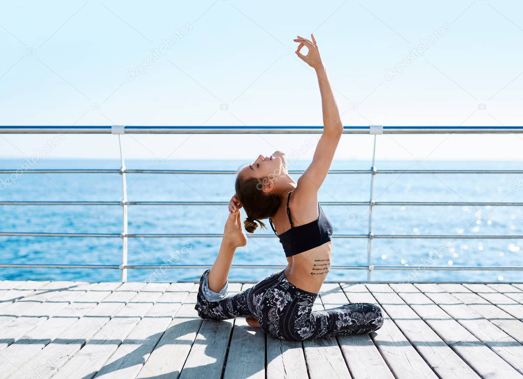 Athletic beautiful young woman sitting in a Pigeon Yoga Pose on the beach against the sea. Feeling so comfortable and relax.
