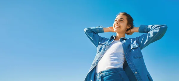 Vista dal basso di una giovane donna attraente sorridente in jeans vestiti nella giornata di sole sullo sfondo del cielo blu . — Foto Stock