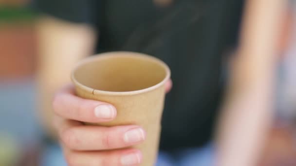 Молодая женщина пьет кофе на открытом воздухе и улыбается. женщина держит бумажную чашку с горячим кофе — стоковое видео