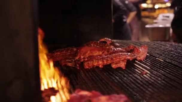 A carne é frita em uma grade grande. costelas de porco assar sobre um fogo em uma grade rotativa enorme — Vídeo de Stock