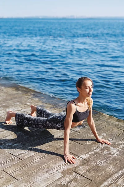 Foto de una joven deportista que hace ejercicios de yoga en la playa con fondo marino. Sentirse tan cómodo y relajarse . — Foto de Stock
