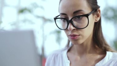 Genç ve güzel bir iş kadını, modern ofiste dizüstü bilgisayarla çalışıyor.