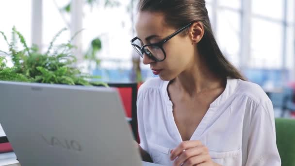 Jonge mooie zakenvrouw werken op laptop in helder modern kantoor — Stockvideo