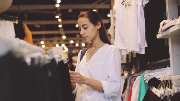 Chica joven buscando ropa en la tienda — Vídeo de stock