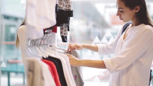 Молодая девушка ищет одежду в магазине — стоковое видео