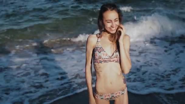 Здоровая женщина с подтянутым телом в моде сексуальная. Модель позирует на фоне моря в лучах заходящего солнца . — стоковое видео