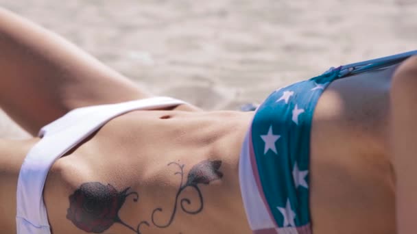 Close-up van fit bikini buik ABS, heupen en benen. slanke mooie dames lichaam op het strand met hemel en zee achtergrond. vrouw ligt op het strand — Stockvideo