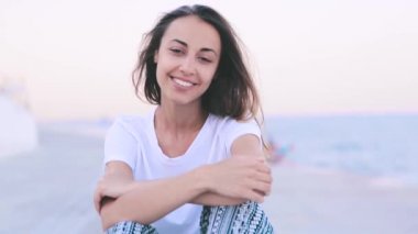 Hafif yaz kıyafetlerine güzel genç kadın şafakta limanda rıhtımda oturuyor. Genç beyaz kadın gün batımı güzel görünümü izliyor.