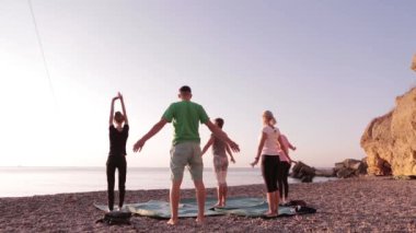 Yoga sınıfı grup yetişkin kadınlar ve bir adam uygulama yoga ve gündoğumu plajda eğitmen ile nefes egzersizleri.