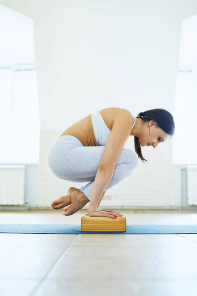 Deportiva mujer joven morena atractiva practicando yoga, haciendo balance de brazos con bloques de yoga en un gimnasio con pared blanca. Estilo de vida saludable, ejercicios matutinos, meditación. Recopilación. Vista lateral — Foto de Stock