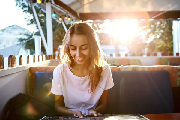 Joven hermosa mujer en camiseta blanca sentada en la cafetería al aire libre con fondo de la puesta del sol . — Foto de Stock