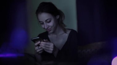 güzel gülümseyen kadın akşam şehir parkında çim oturur, elinde bir telefon tutar, swiping, mesajları okuma ve arama