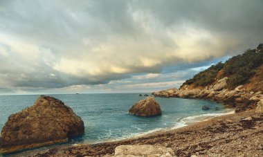 Bulutlu gökyüzü ile harika bir sahil. Gün batımında mavi deniz bitiyor. Güzel sahil koyunun manzarası. Yaz zamanı..