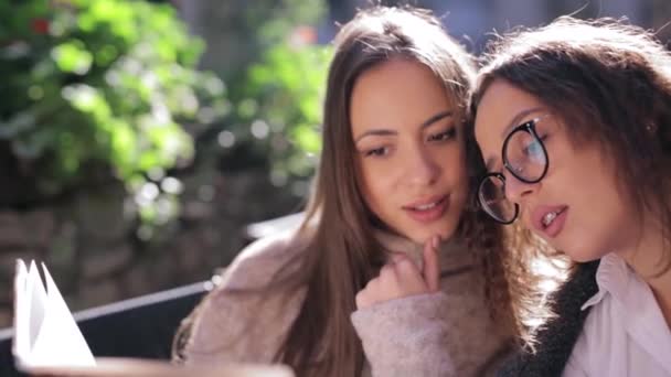 Duas mulheres bonitas jovens que olham para o menu no restaurante, virando páginas e escolhendo pratos para o café da manhã — Vídeo de Stock