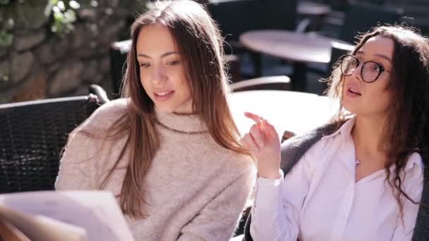 Две молодые красивые женщины смотрят меню в ресторане, переворачивают страницы и выбирают тарелки на завтрак — стоковое видео