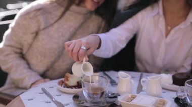 kafe veya restoranda masada oturan ve kahvaltı iki güzel genç kadın. kahve fincanı bir süt döken kadın