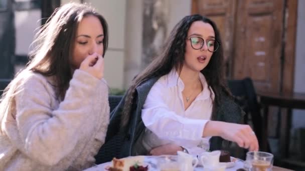 Two beautiful young women sitting at the table in cafe or restaurant and having breakfast. woman pouring a milk to the cup of coffee — Stock Video