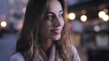 Çekici zarif Kadın Kamera ve Gülümseyen yan bakar. ışıklar ile closeup akşam şehir portresi