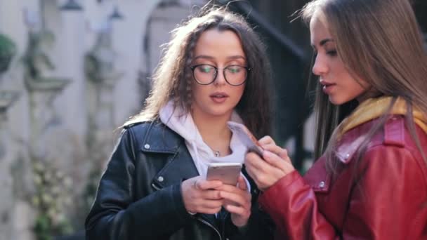 Duas meninas usando telefones inteligentes ao ar livre. Duas mulheres compartilham dados ou contatos em smartphones — Vídeo de Stock