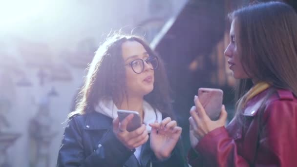 Deux jeunes filles utilisant des téléphones intelligents à l'extérieur. Deux femmes partagent des données ou des contacts dans des smartphones — Video