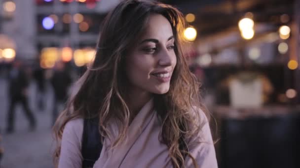 Aantrekkelijke elegante vrouw kijkt aan de zijkant van de camera en glimlachend. Close-up avond stad portret met verlichting — Stockvideo