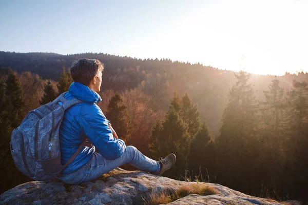 Mennesket sitter på klippekanten mot soloppgangens bakgrunn . – stockfoto