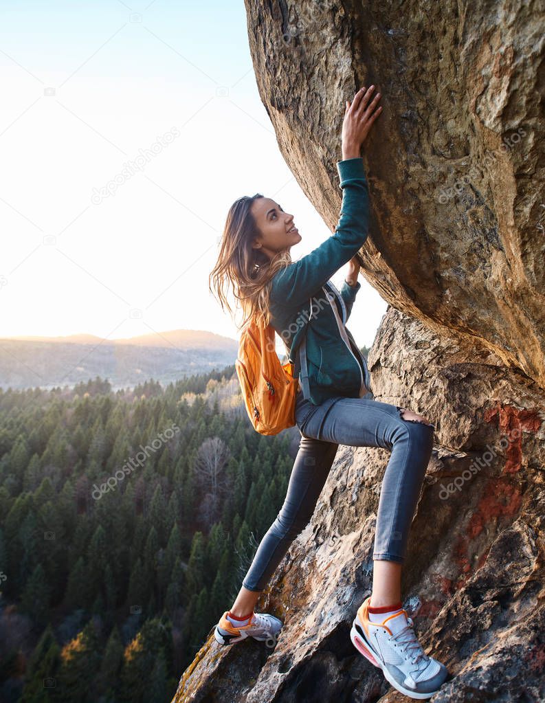 young attractive woman hiker climbing on the rock at sunset