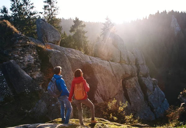 To reisende som sto på klippen mot skogkledde åser og skyet himmel ved soloppgang. Et par stående hender, hilser på solen . – stockfoto