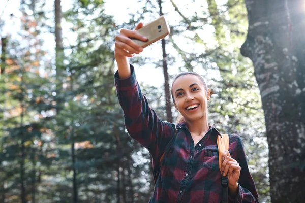 Vakker, stilfull, reisende kvinne som tar bilde på kameratelefonen med skogbakgrunn . – stockfoto