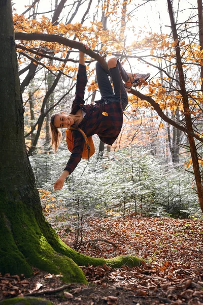 Joven mujer feliz colgando en el árbol iand ríe n bosques con mochila naranja. Divertida chica tonteando sobre un fondo de bosque . — Foto de Stock