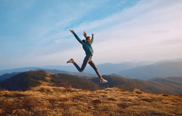 Happy woman hiker jumping on mountain ridge on blue cloudy sky and mountains background. — 图库照片