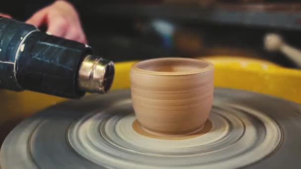 O oleiro com um secador industrial seca um vaso de barro em uma roda de oleiros. Olaria artesanal dentro . — Vídeo de Stock