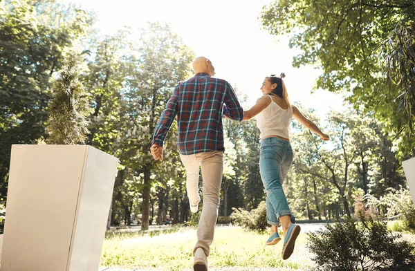 Joven pareja feliz corriendo por el parque. Un par en movimiento. Vista trasera . —  Fotos de Stock