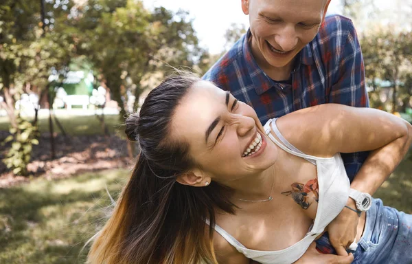 Immagine ravvicinata di una giovane coppia che si diverte e ride nel parco. Fidanzato abbraccia la sua ragazza da dietro . — Foto Stock