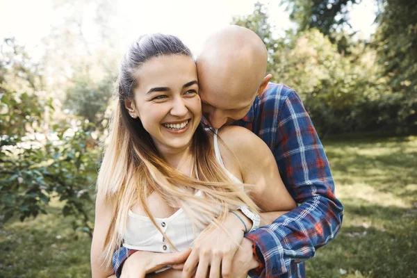 Giovane coppia divertirsi e ridere nel parco. Fidanzato abbraccia la sua ragazza da dietro . — Foto Stock