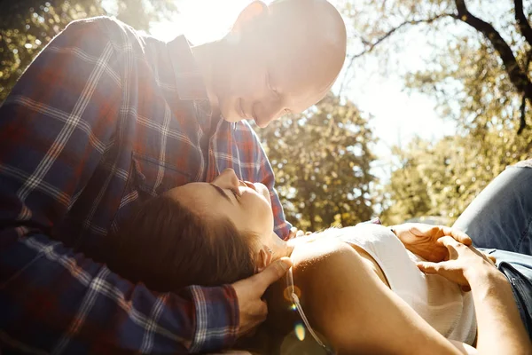 Aşık genç çift parkta vakit geçirir. Genç bir kadın erkeğin dizlerinin üzerine çöküp birbirine güneş ışınlarıyla bakıyor.. — Stok fotoğraf