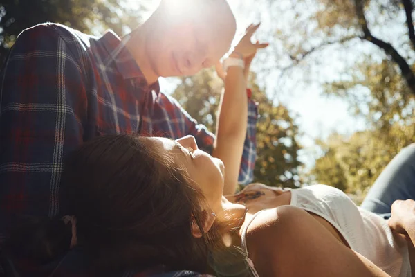 恋爱中的年轻夫妇在公园里消磨时间。 年轻的女人跪在男人的膝上，面面相觑，背负着太阳光. — 图库照片