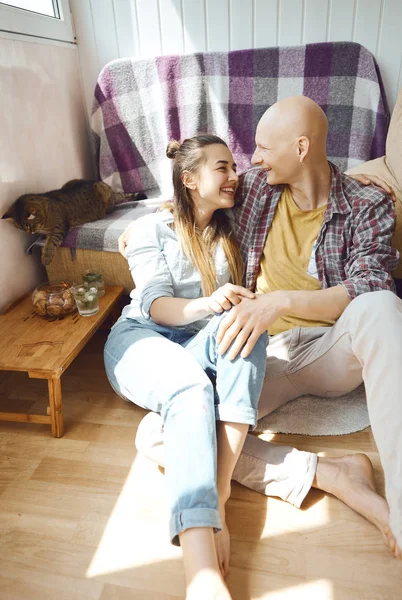 Ungt smilende par som tilbringer tid sammen hjemme, sitter på gulvet på soverommet, klemmer hverandre . – stockfoto