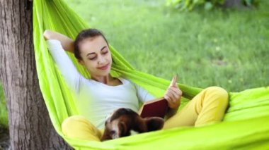 sevimli Galler Corgi köpek parkta parlak yeşil hamak yalan ve bir kitap okuma ile çekici genç kadın.
