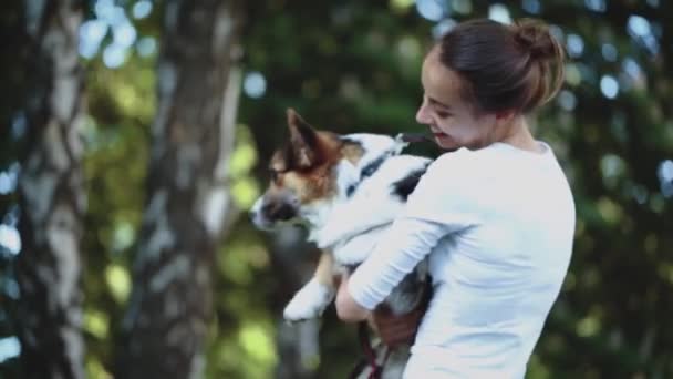 Молодая красивая улыбающаяся женщина с милой валлийской собакой Корги, лежащей в ярко-зеленом гамаке в парке — стоковое видео